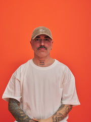 Man wearing a beige cap and white t-shirt against an orange background