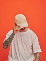 Person wearing a cream cap and white t-shirt against an orange background
