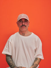 Man wearing a pink cap and white t-shirt against an orange background