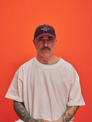 Person wearing a white t-shirt and dark cap against an orange background