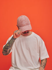 Person wearing a pink cap and white t-shirt against an orange background