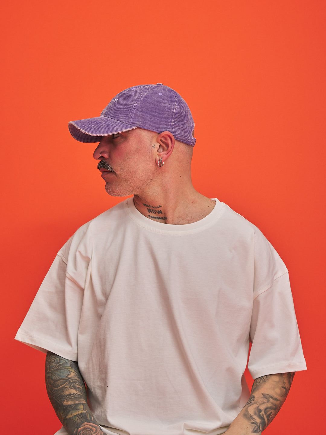 Person wearing a purple cap and white t-shirt against an orange background