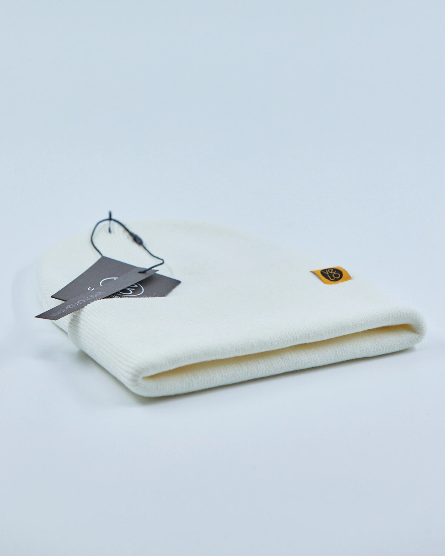 White beanie with a tag and logo on a light gray background