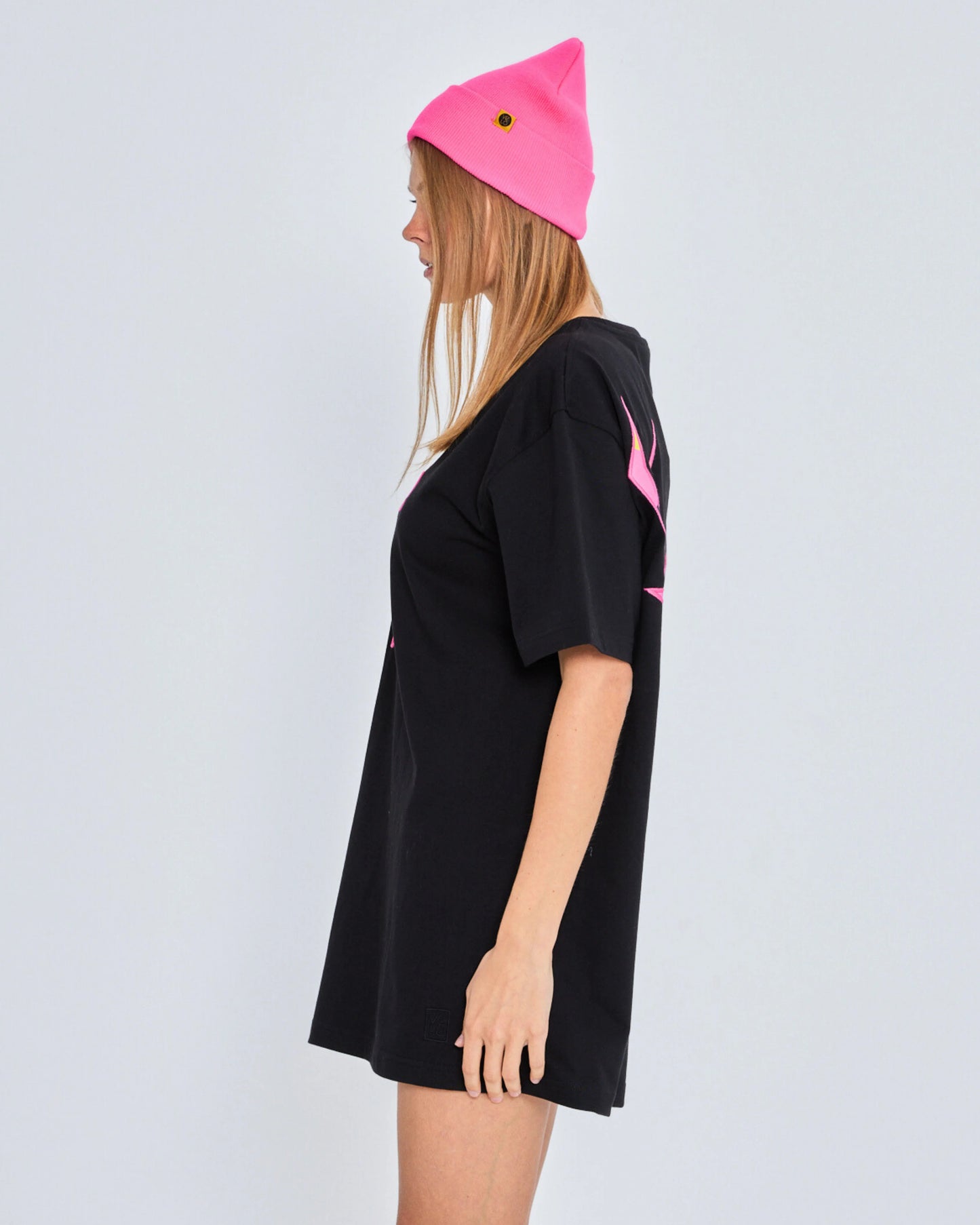 Person wearing a black oversized t-shirt with pink logo and a pink beanie on a light gray background