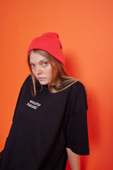 Person wearing a black oversized t-shirt with text and a red beanie against an orange background