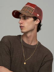 Man wearing Royalty Brick Trucker Hat and brown sweater with a gold chain necklace on a gray background