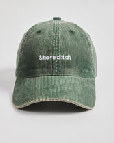 Green corduroy cap with 'Shoreditch' text on a light gray background