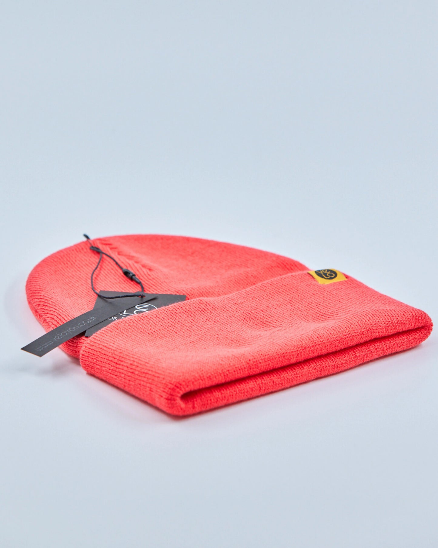 Tomato red beanie with a tag on a light gray background
