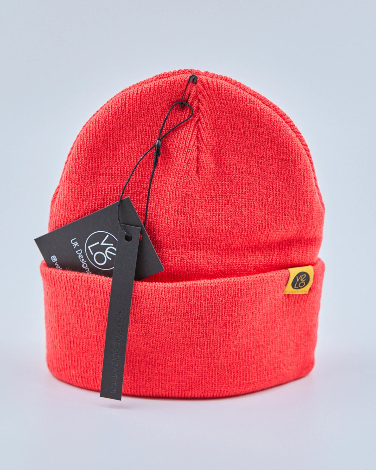 Tomato red beanie with a brand tag on a light gray background