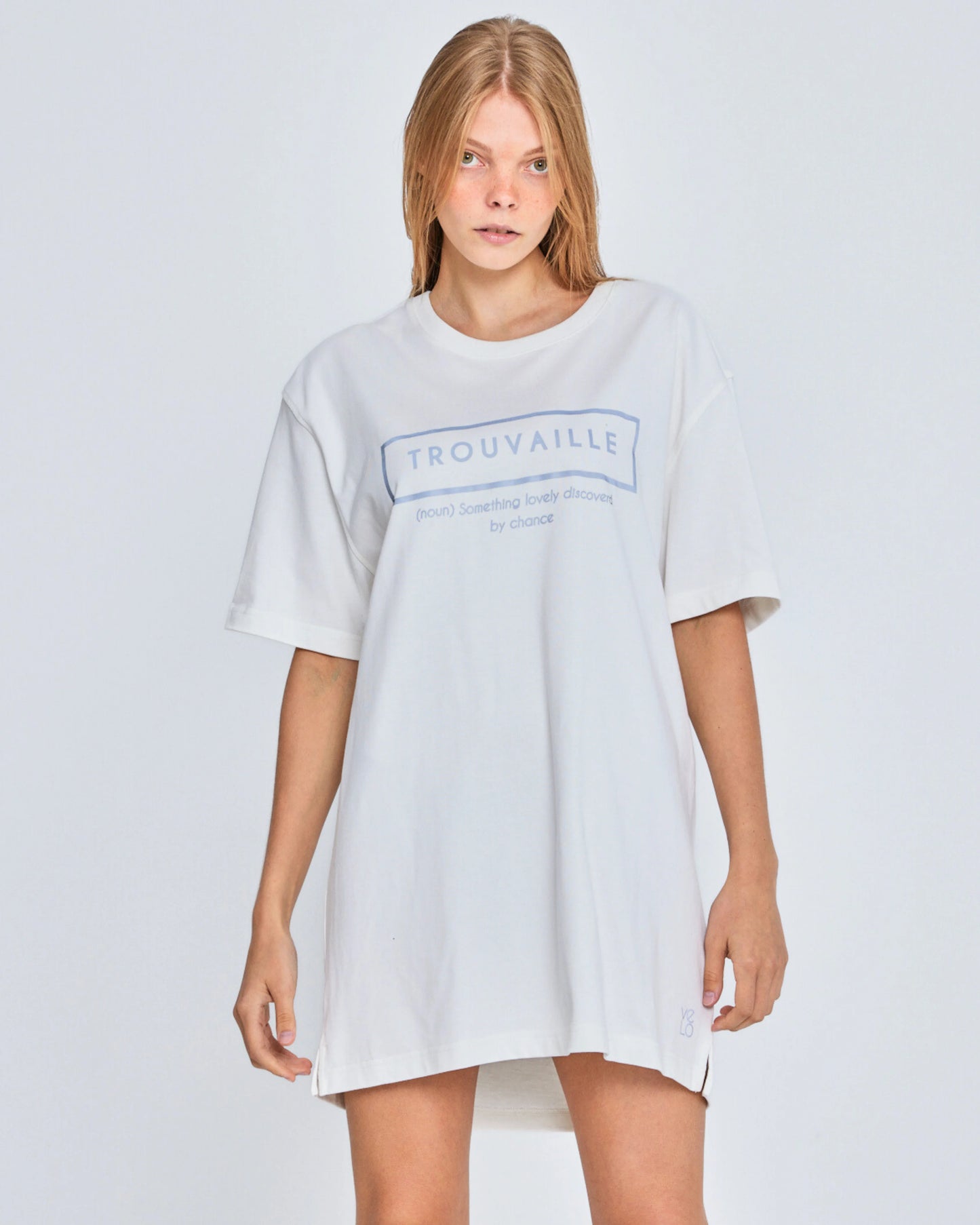 Person wearing a white oversized t-shirt with 'Trouvaille' logo on a light gray background