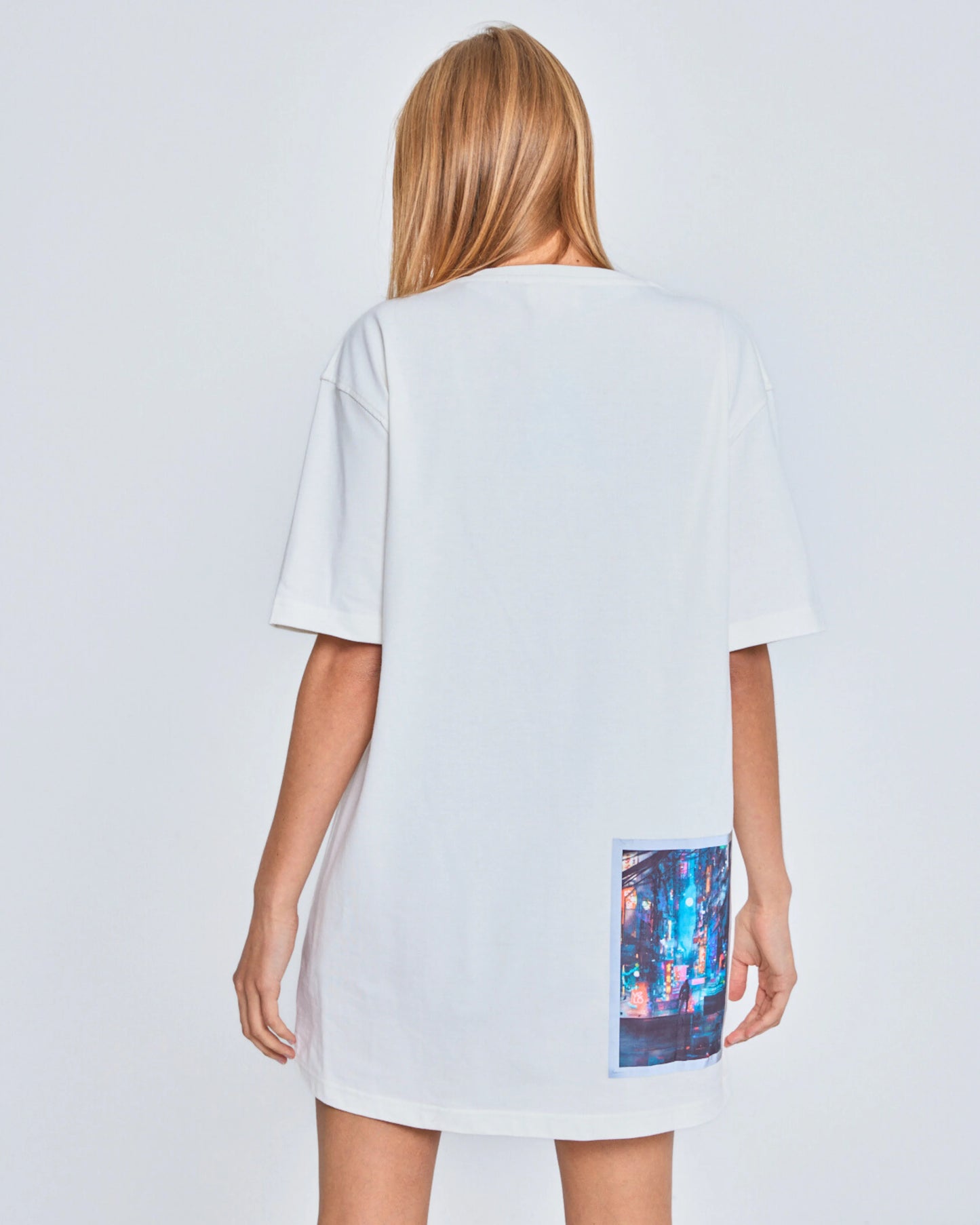 Person wearing a white dress with a colorful pocket design on a plain background