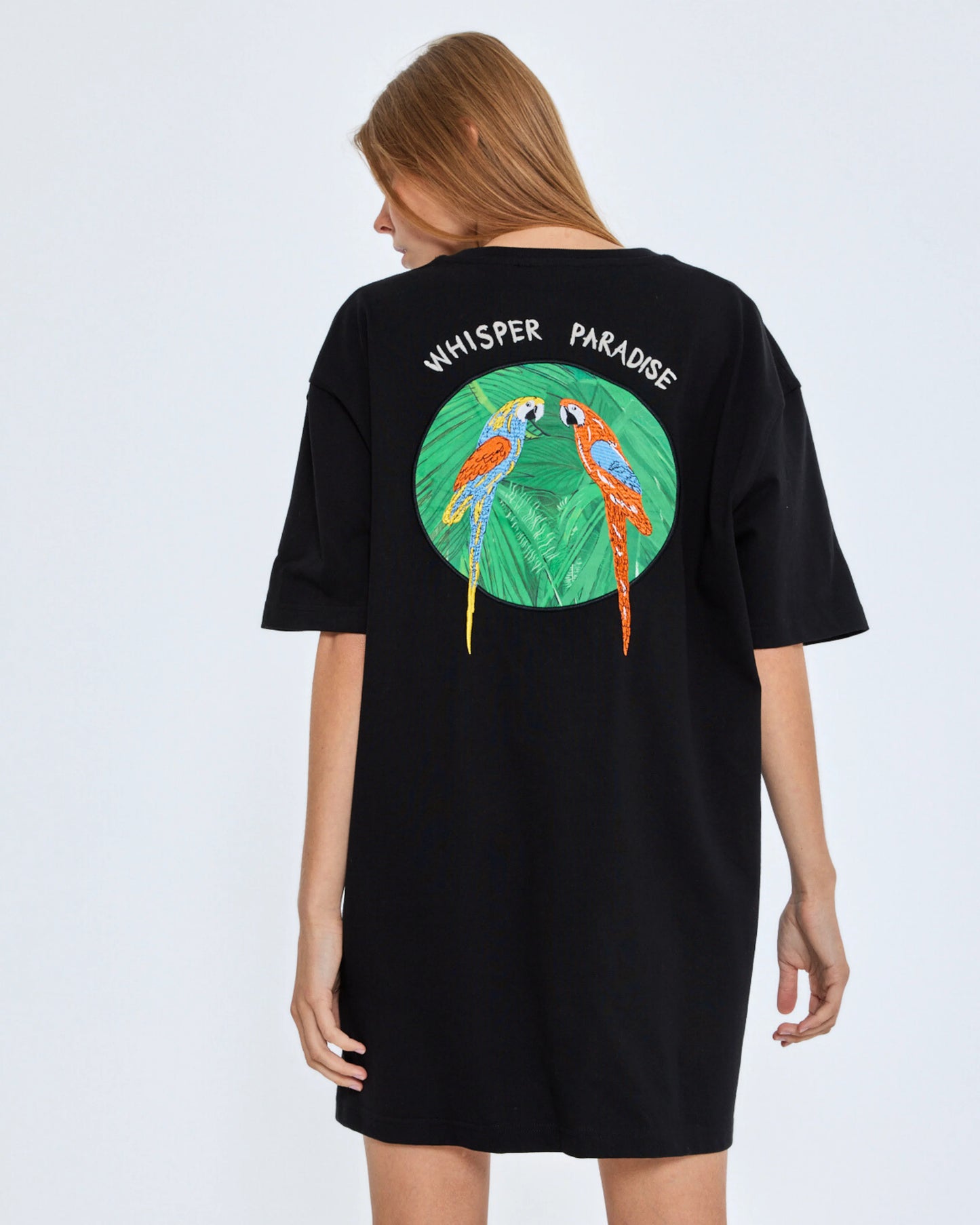 Black t-shirt with parrot design and 'Whisper Paradise' text on a white background