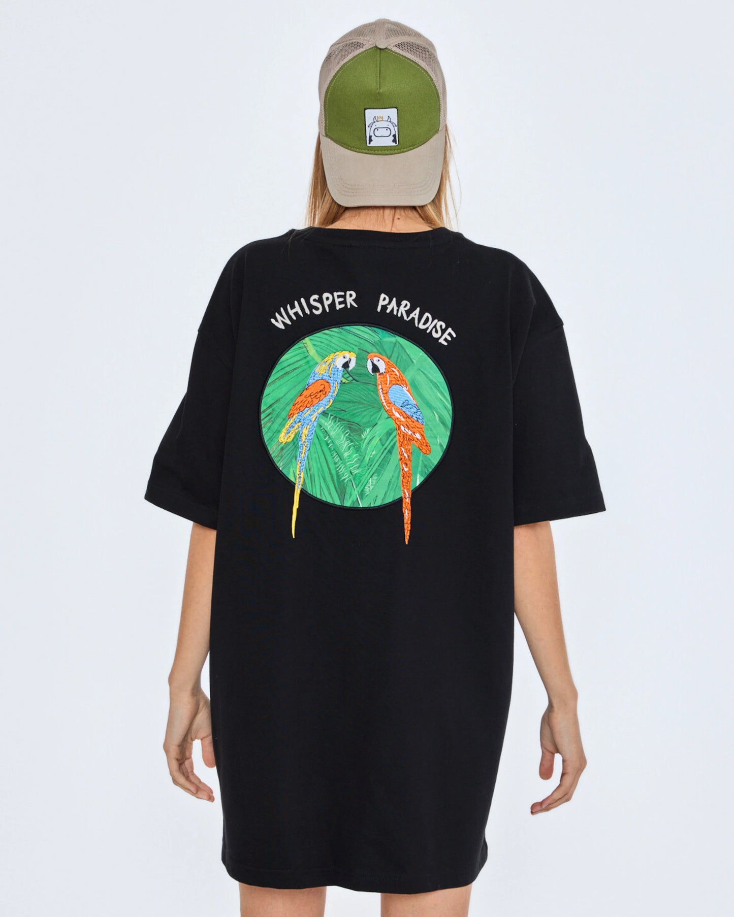 Black t-shirt with parrot design and 'Whisper Paradise' text on the back, worn by a person.