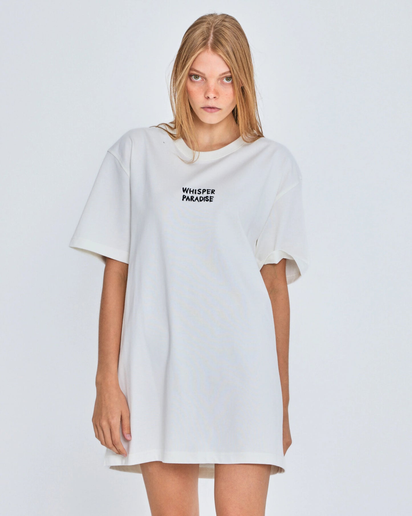 Woman wearing a white oversized t-shirt with text on a plain background