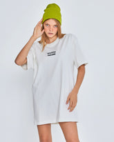 Person wearing a white oversized t-shirt with text and a green beanie on a plain background