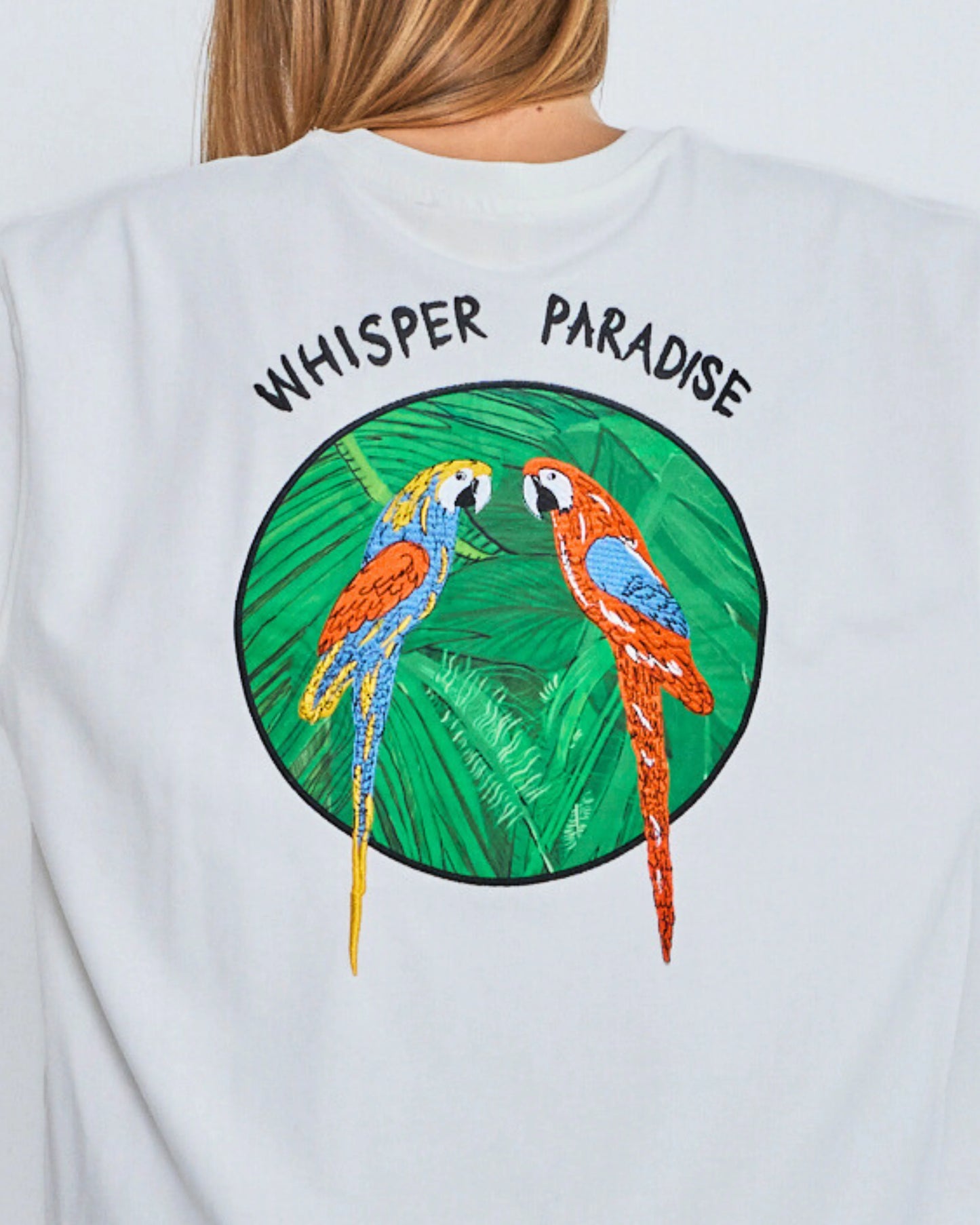 White sweatshirt with parrot design and 'Whisper Paradise' text on a plain background