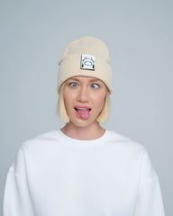 A person wearing a beige beanie hat with a 'cow' design on the cuff, paired with a white t-shirt.