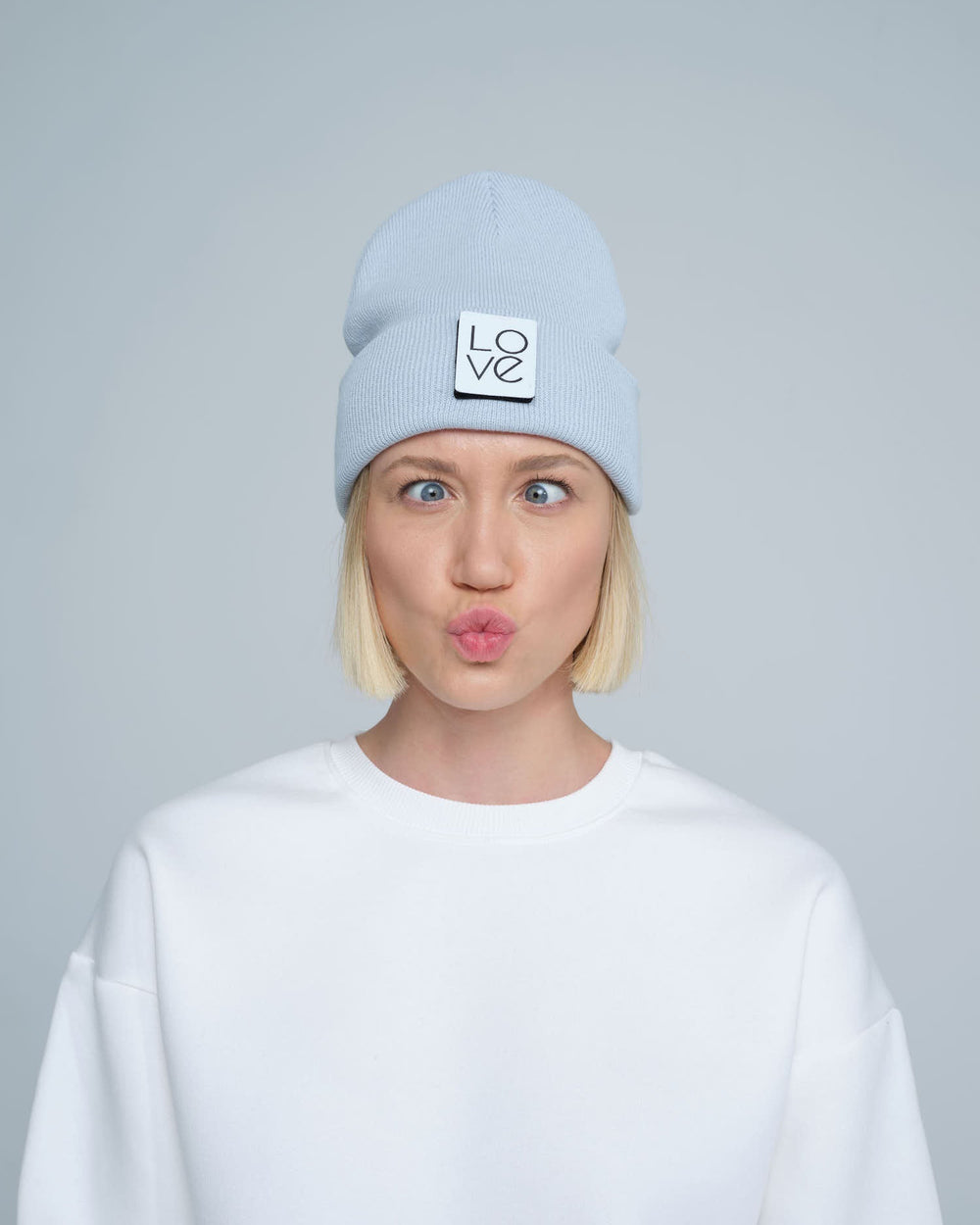 A person wearing a baby blue beanie with a 'Love' text design patch on the front.