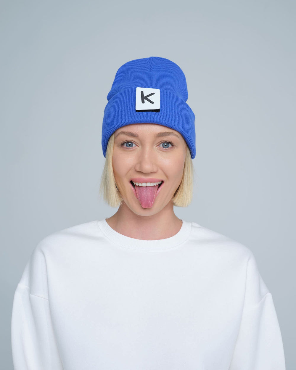 female model wearing blue beanie with K letter patch on it and making a funny face