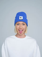 female model wearing blue beanie with K letter patch on it and making a funny face