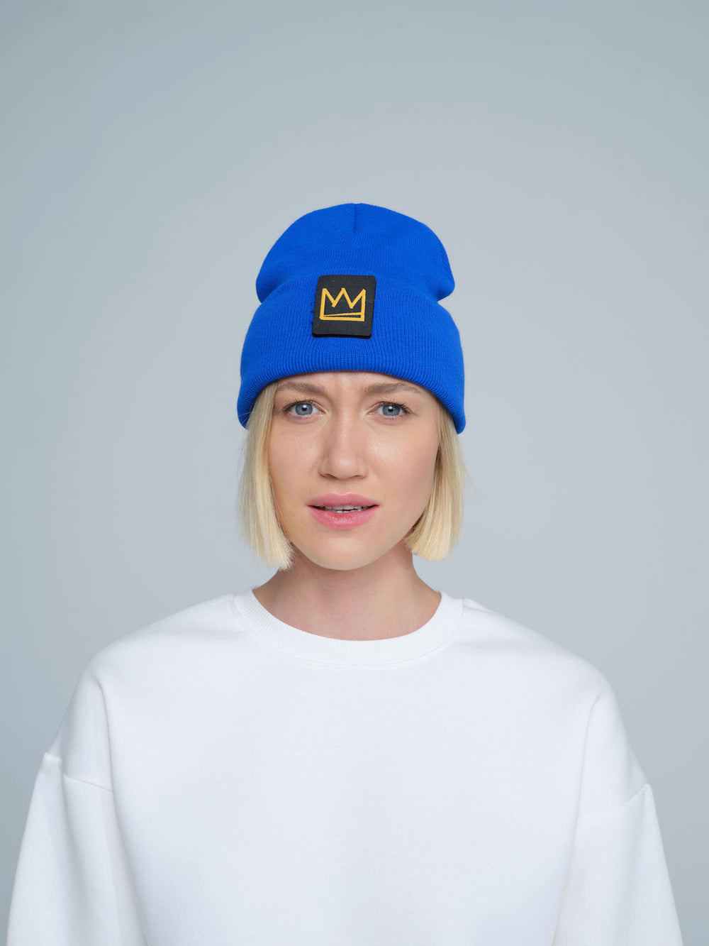 A female person wearing a cobalt blue beanie with a crown design patch on the front.