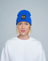 A female person wearing a cobalt blue beanie with a crown design patch on the front.