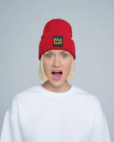 A person wearing a red beanie with a 'crown' design on the cuff, and a white t-shirt.