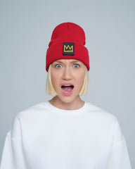 A person wearing a red beanie with a 'crown' design on the cuff, and a white t-shirt.