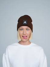 A person wearing a dark brown beanie with a 'A' letter design patch on the front.