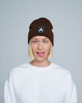 A person wearing a dark brown beanie with a 'A' letter design patch on the front.