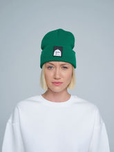 female model wearing dark green beanie with a 'duck' patch on the front