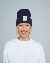 A woman wearing a dark slate navy beanie with a design on the cuff, and the brand logo 'Velo' on the fold.