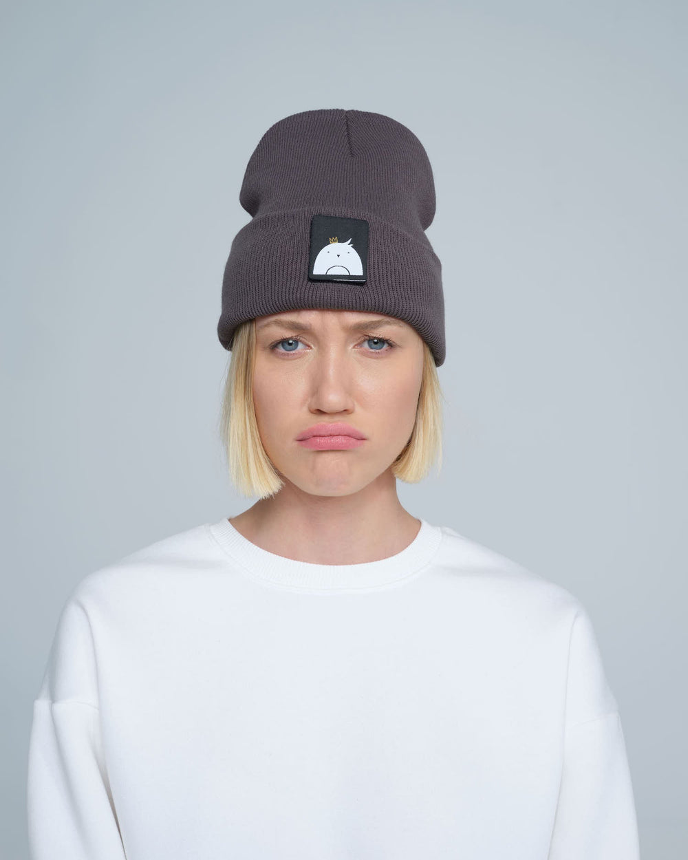 A person wearing a dim gray beanie hat with a 'bird' design patch on the front.