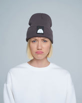 A person wearing a dim gray beanie hat with a 'bird' design patch on the front.