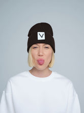 A person wearing an espresso beanie hat with a 'V' letter design on the cuff, and a white t-shirt.