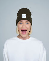 A person wearing a forest green beanie with a design on the cuff, paired with a white t-shirt.