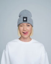 female model wearing grey beanie with 'e' letter design patch on the front