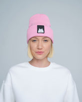 A person wearing a pink beanie with a cat design patch on the front.