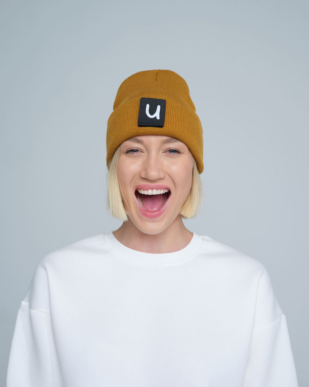 female model wearing peru colour patch ready beanie with 'u' letter on it and smiling