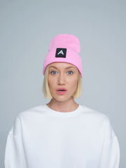 A person wearing a pink beanie with a design on top and the letter 'A' on it, paired with a white crew neck sweater.