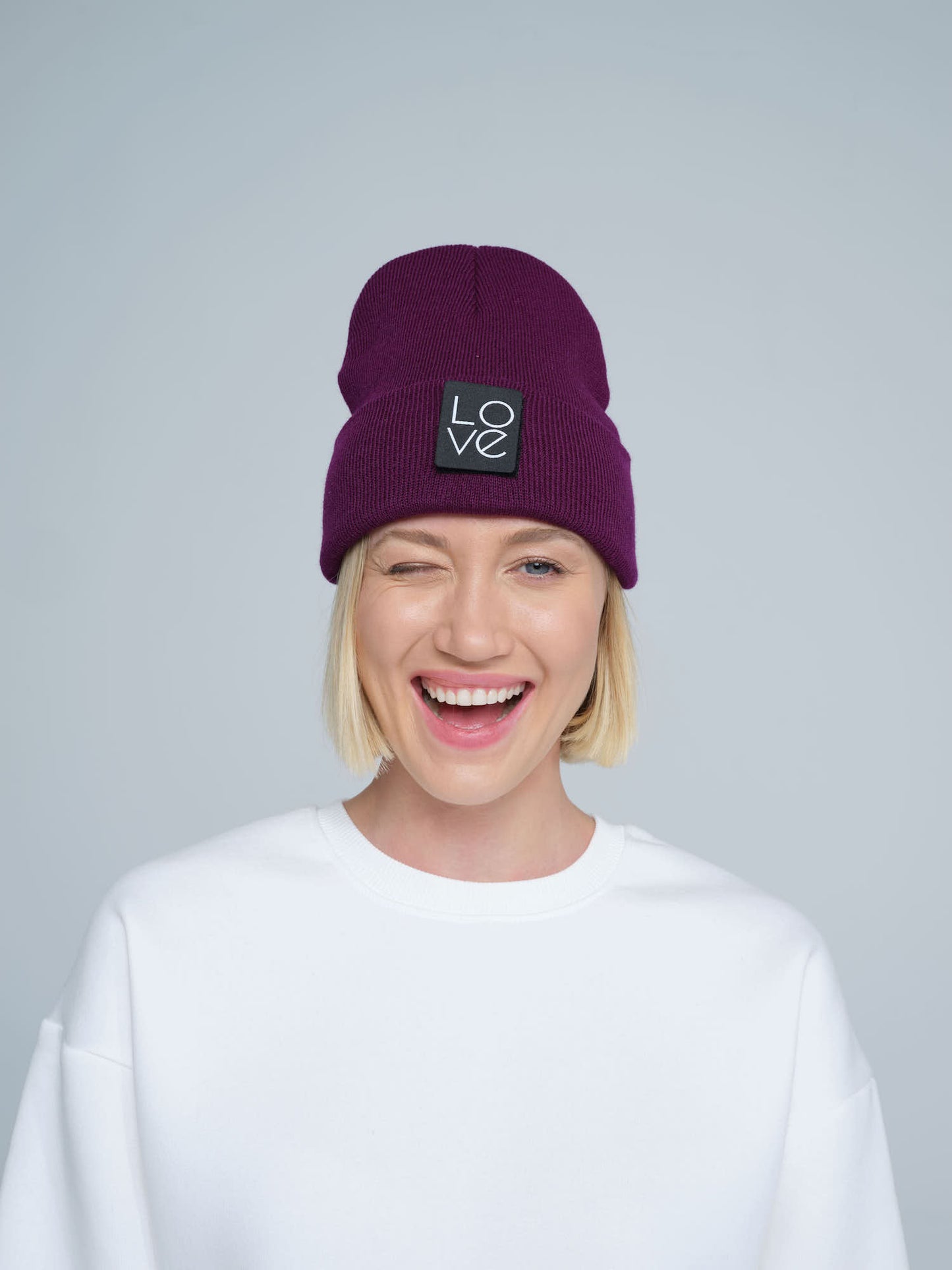 A person wearing a purple beanie hat with a 'Love' logo on the front with a smiling face.