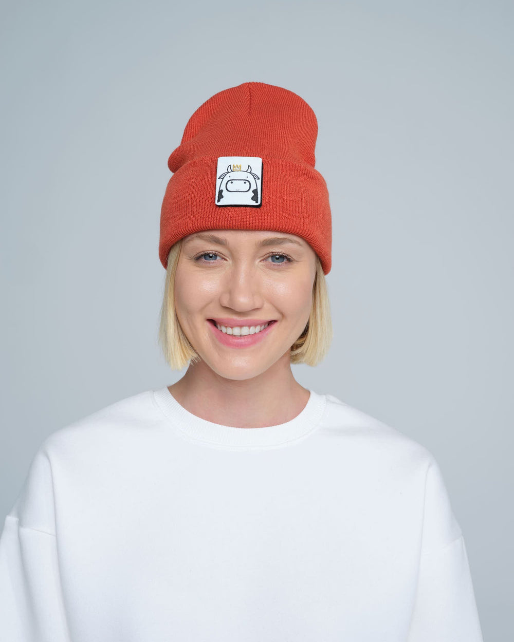 A person wearing a rust orange beanie hat with a cow design patch on the front.