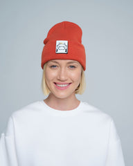 A person wearing a rust orange beanie hat with a cow design patch on the front.