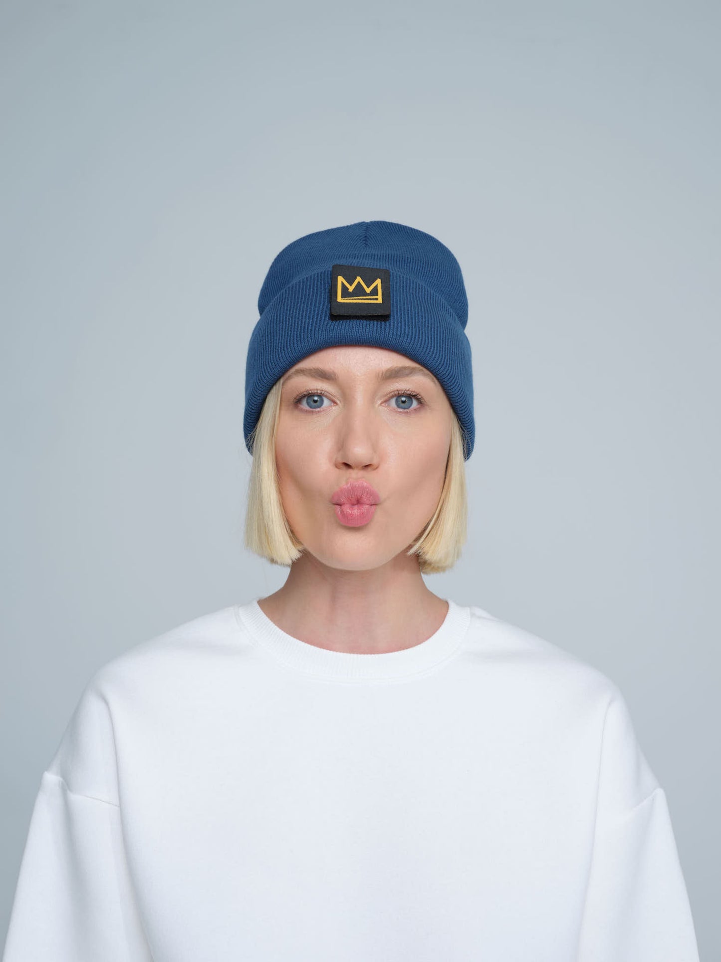 female model wearing steel blue beanie with a crown patch on it with a funny face