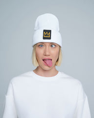 A female wearing a white beanie with a crown symbol on it, standing in a funny pose.