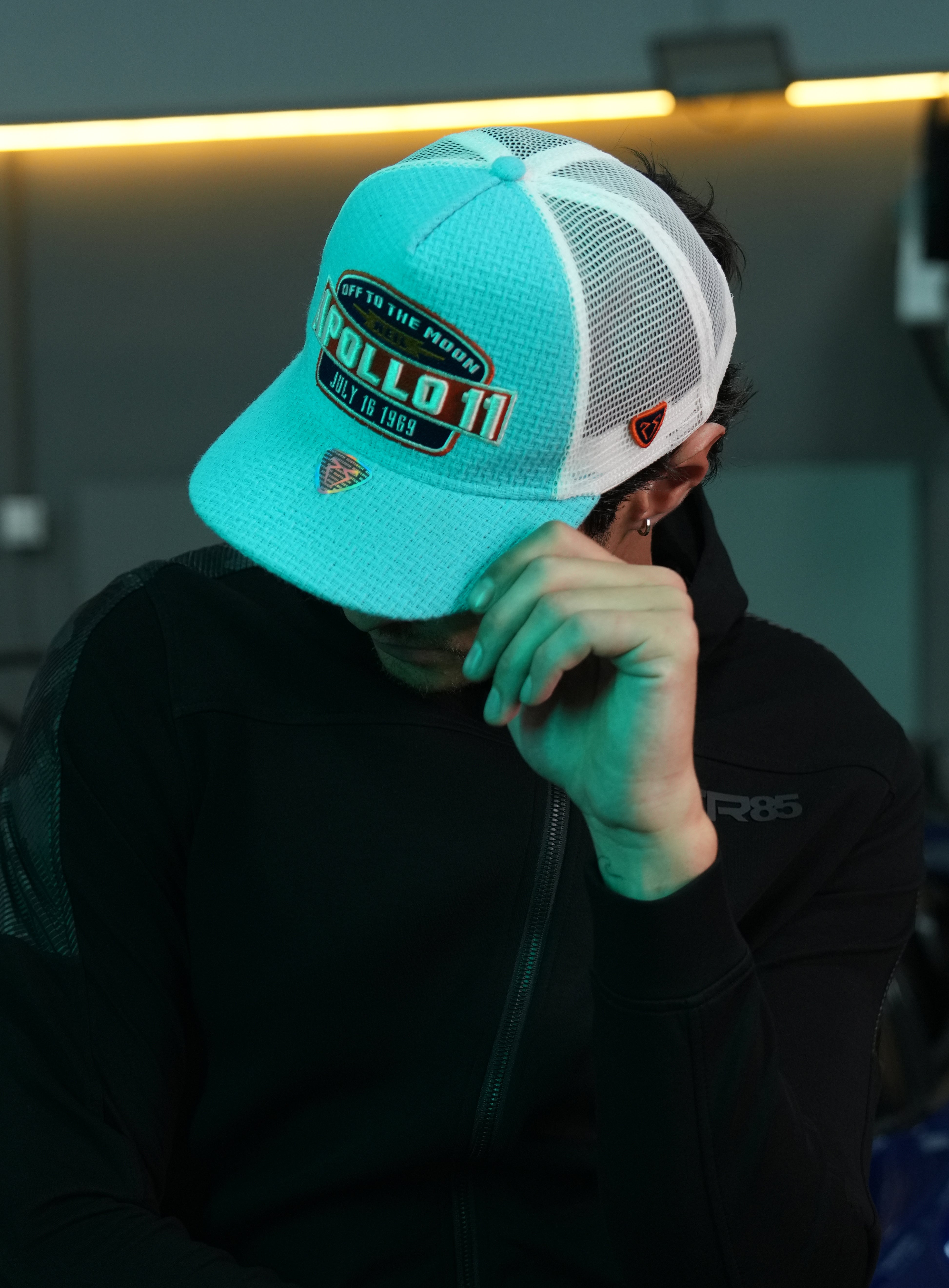 Person wearing Apollo Blue Trucker Hat, sitting indoors.