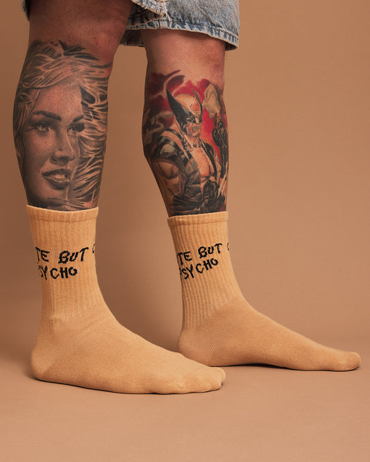 Beige socks with text worn by a person with tattoos on a brown background