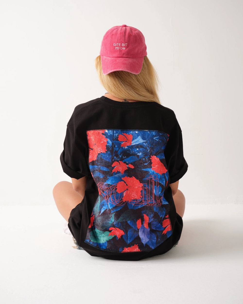 Person wearing a black t-shirt with colorful floral design on the back, sitting against a white background.