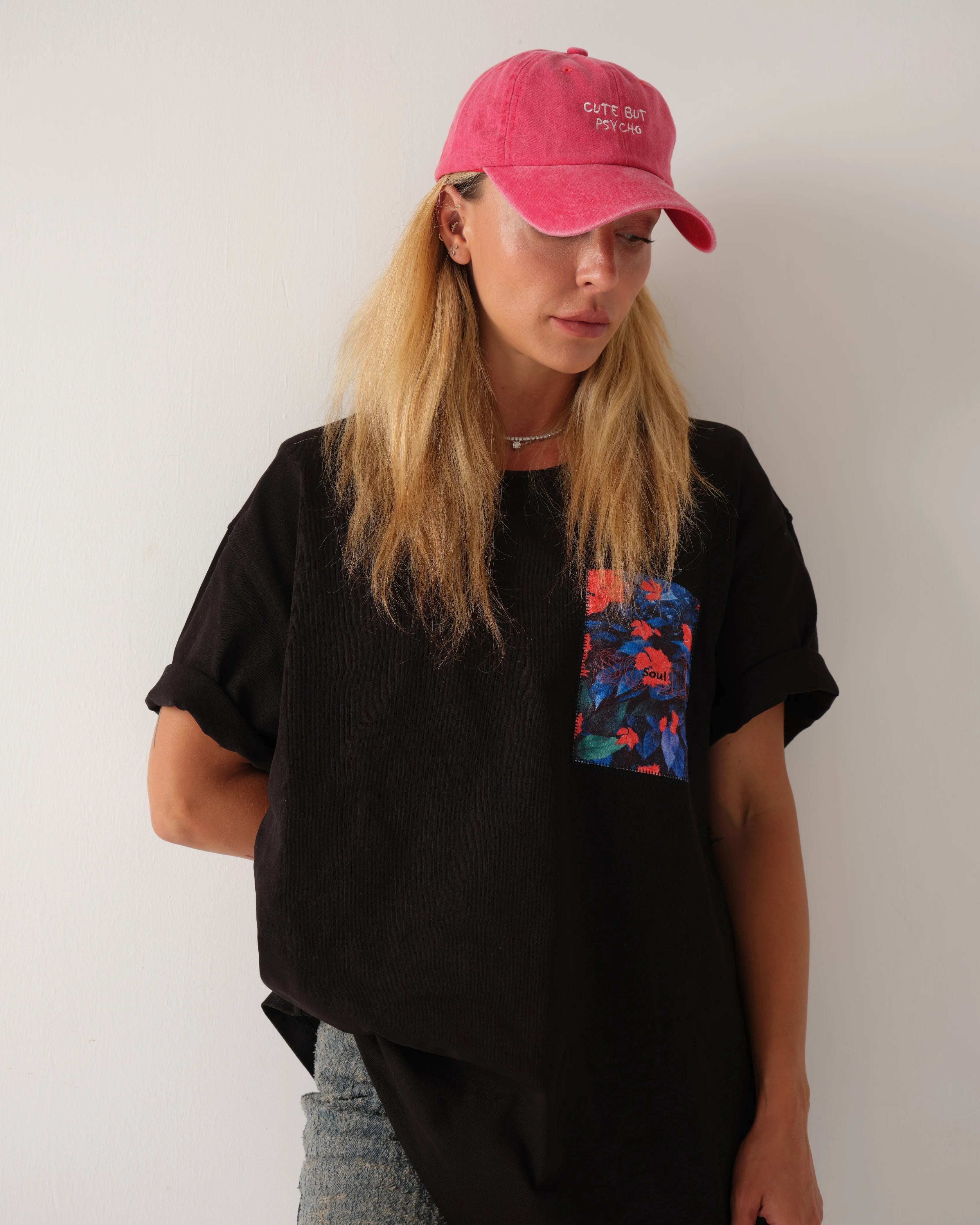 Person wearing a black t-shirt with a colorful pocket design and a pink cap against a plain background