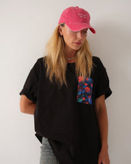 Person wearing a black t-shirt with a colorful pocket design and a pink cap against a plain background